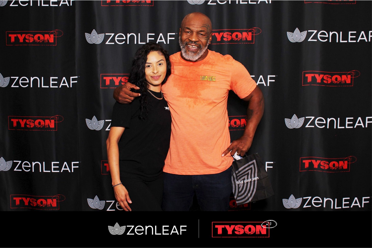 Mike Tyson in an orange shirt and a woman in a black shirt pose at the activations photo booth, featuring ZenLeaf and Tyson logos on the black backdrop. Both smile warmly at the camera.