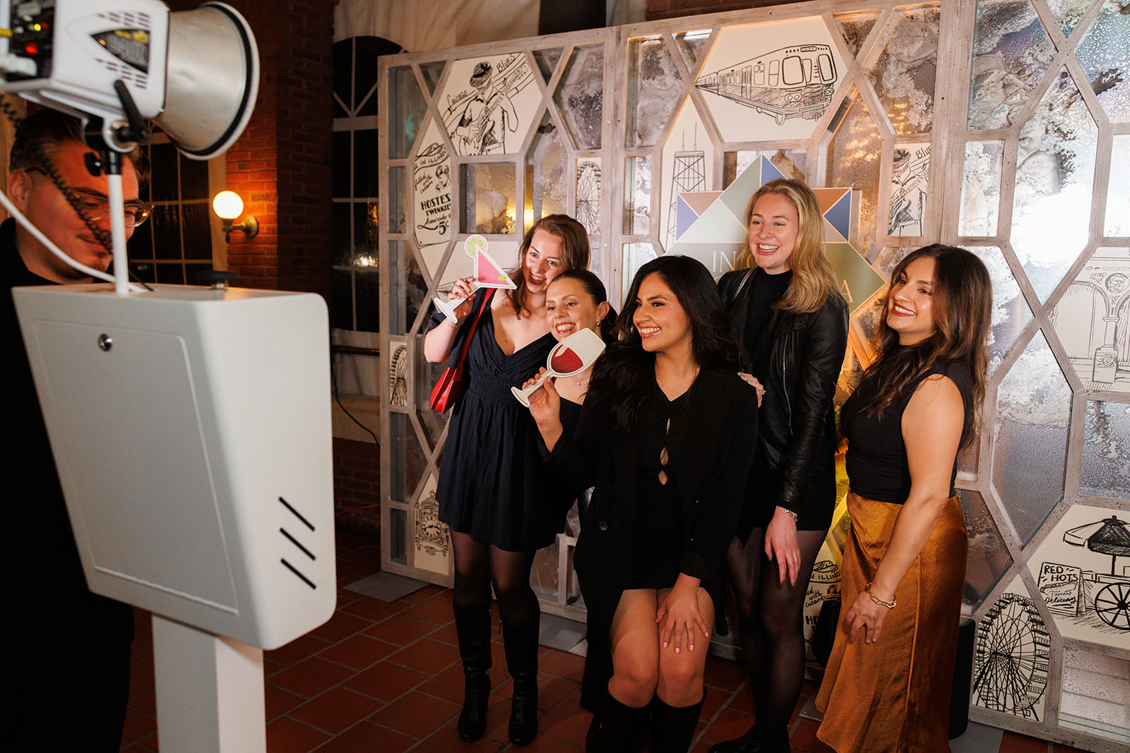 Five people smiling and posing for a group photo in front of a decorative backdrop at a Chicago party event. They are holding photo booth props from Shutterbox Entertainment and appear to be having a fun time with the modern photo booth experience.