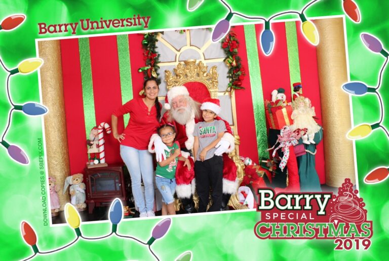 A woman and two children pose with Santa Claus in a festive setting at the university holiday photo booth. The scene includes Christmas decorations and gifts, with a green border adorned by colorful lights. The text reads Barry University and Barry Special Christmas 2019.