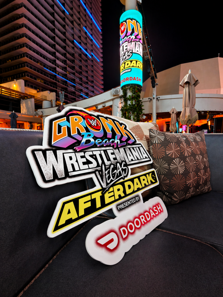 Foam signs for WWE Gronk Beach, WrestleMania Vegas After Dark, and DoorDash rest on a lounge chair; Glambot brand activation Las Vegas branding lights up a tall screen at this vibrant night event.