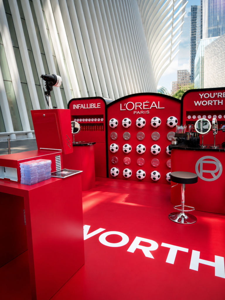 A red L'Oréal Paris booth with makeup, mirrors, a ring light, and soccer ball wall—a modern space perfect for Brand Activation Photo Booth moments.