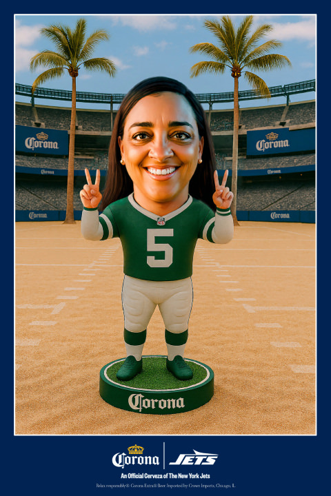 A bobblehead figure in a New York Jets football uniform stands on a sandy football field, holding up two peace signs, with Corona branding and palm trees in the background.