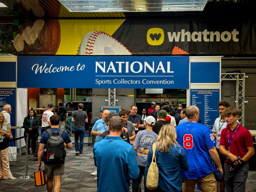 People gather at the entrance of the National Sports Collectors Convention under a large welcome sign, with an Experiential Marketing whatnot banner above.