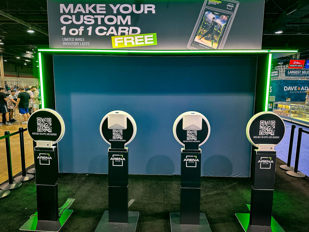 Four kiosks with QR codes stand under a sign offering free custom 1 of 1 cards—a creative example of experiential marketing—inside an indoor event space bustling with people.