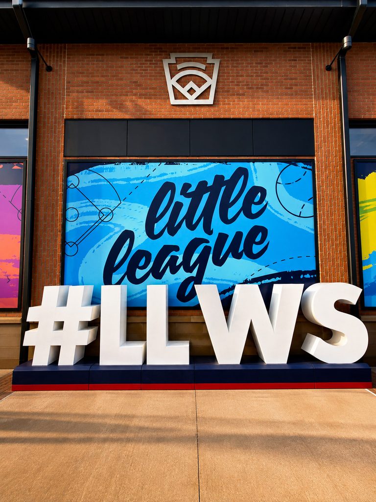Large white letters spell #LLWS in front of a colorful Little League sign—perfect for Arena Club or Trading Card Photo Booth Rental at The National Sports Collectors Convention.